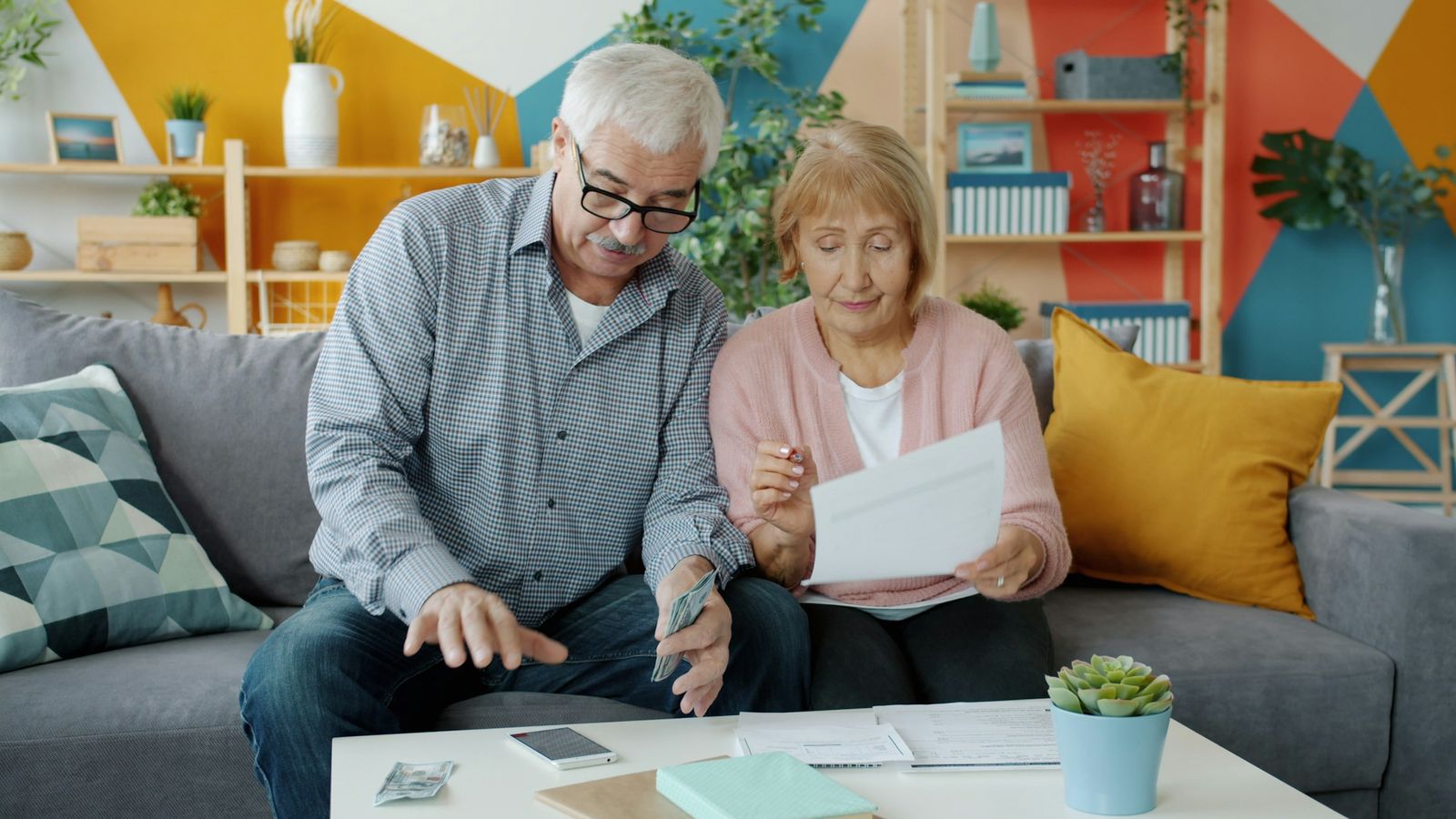 An older couple on a sofa going through papers and bills together at a coffee table.