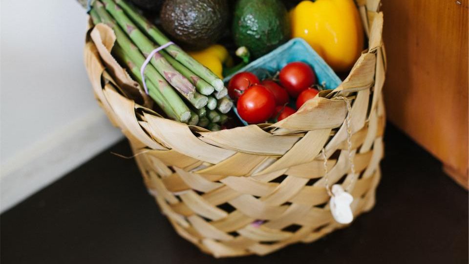 A woven grocery basket full of fresh vegetables and fruit.