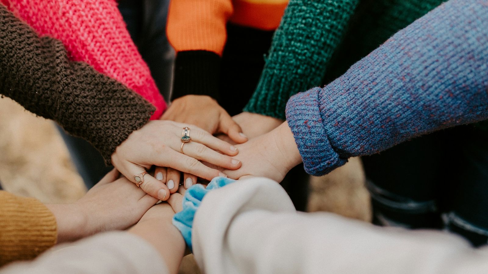 Co-workers in colorful sweaters stack their hands together in a circle.