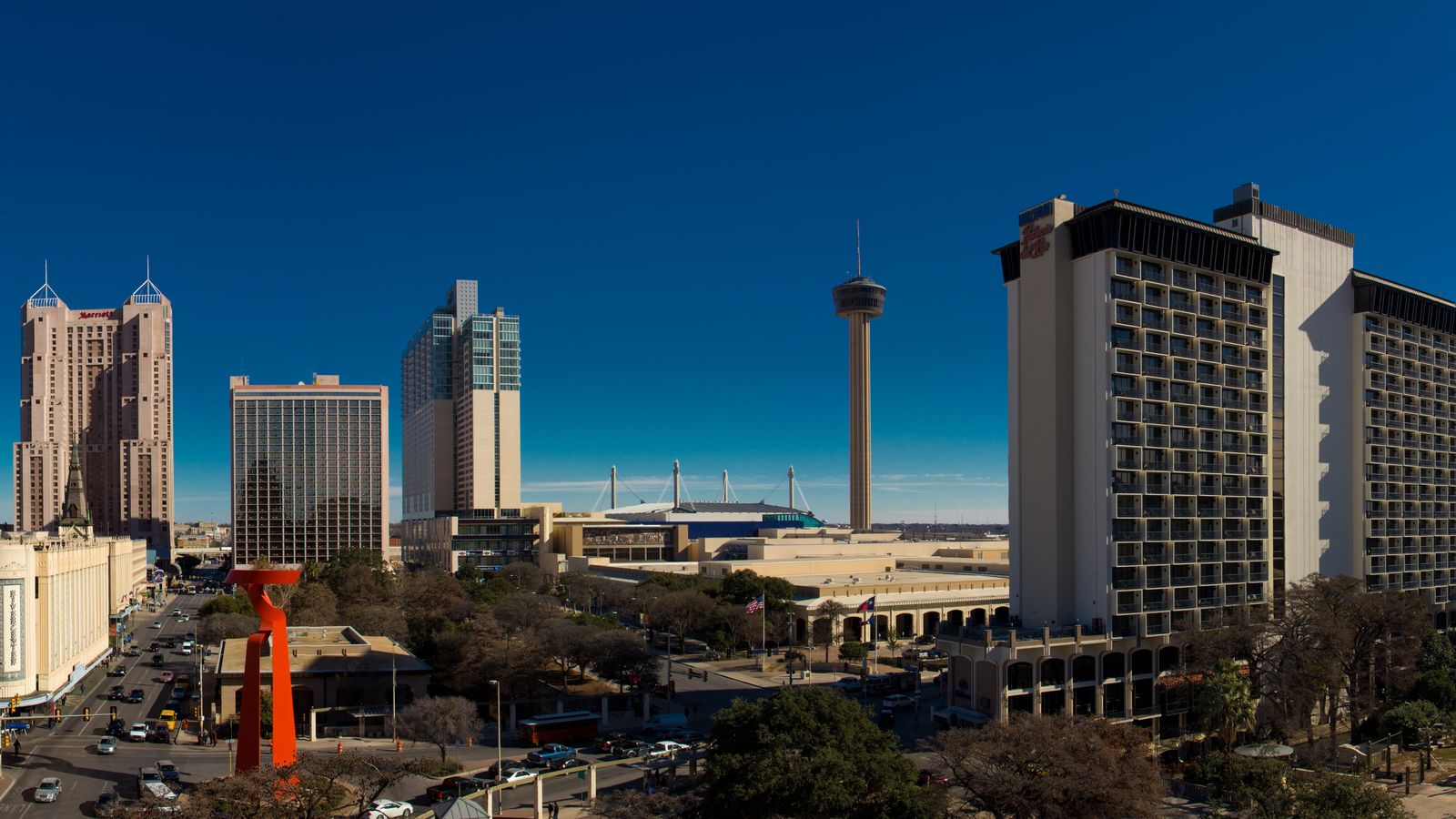 Downtown San Antonio under a deep blue sky, with the Tower of the Americas and the hotel towers rising above the streets.