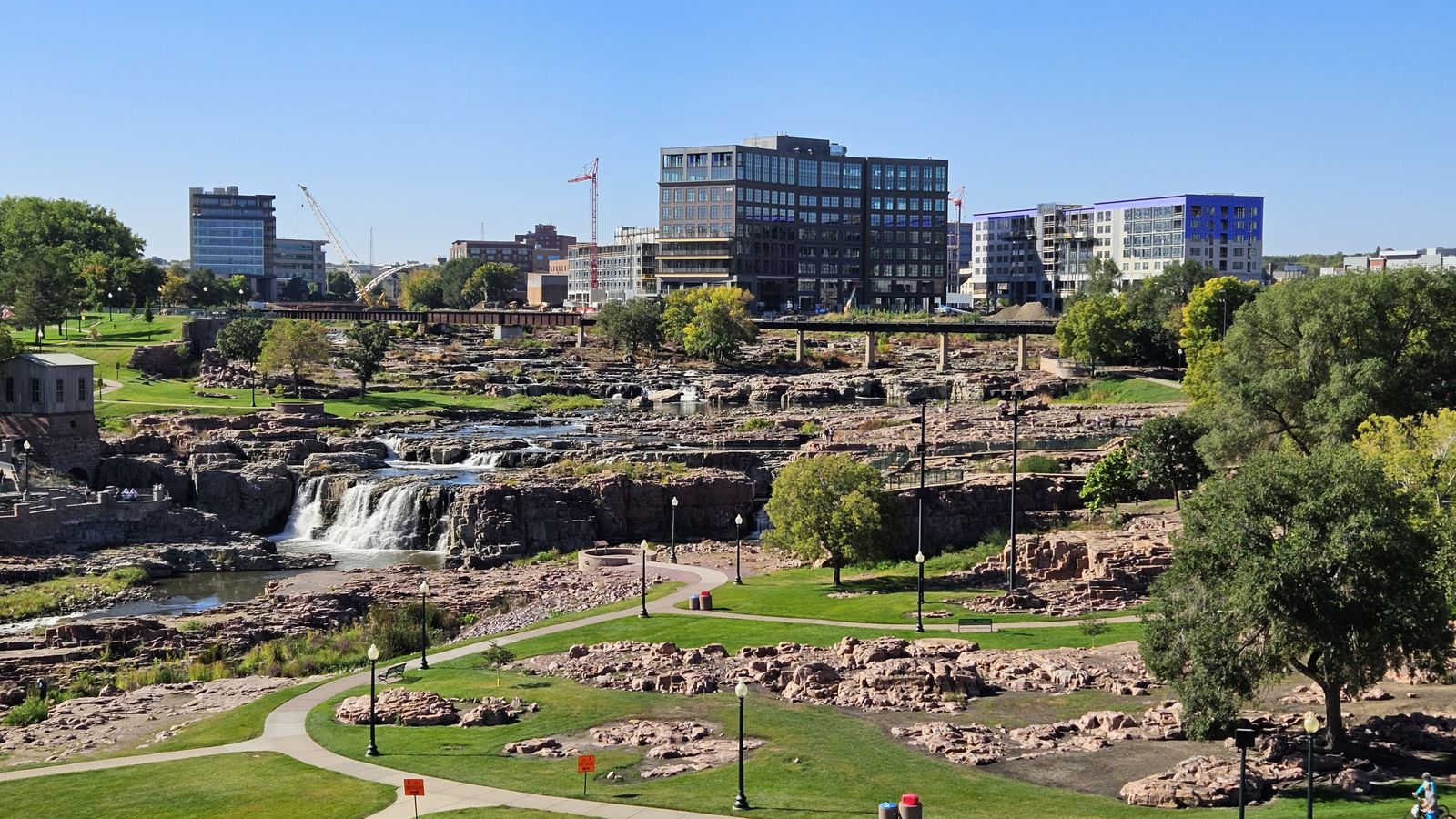 Falls Park in Sioux Falls, with the falls of the Big Sioux River in the foreground and the downtown buildings behind.