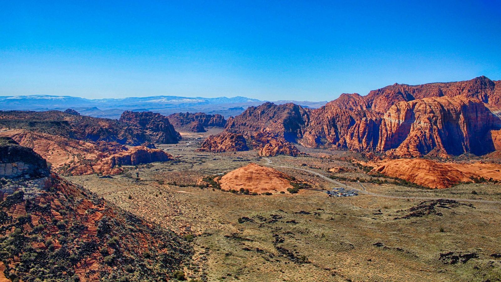 The red and white sandstone cliffs of Snow Canyon under a clear blue sky, with the desert valley floor below.