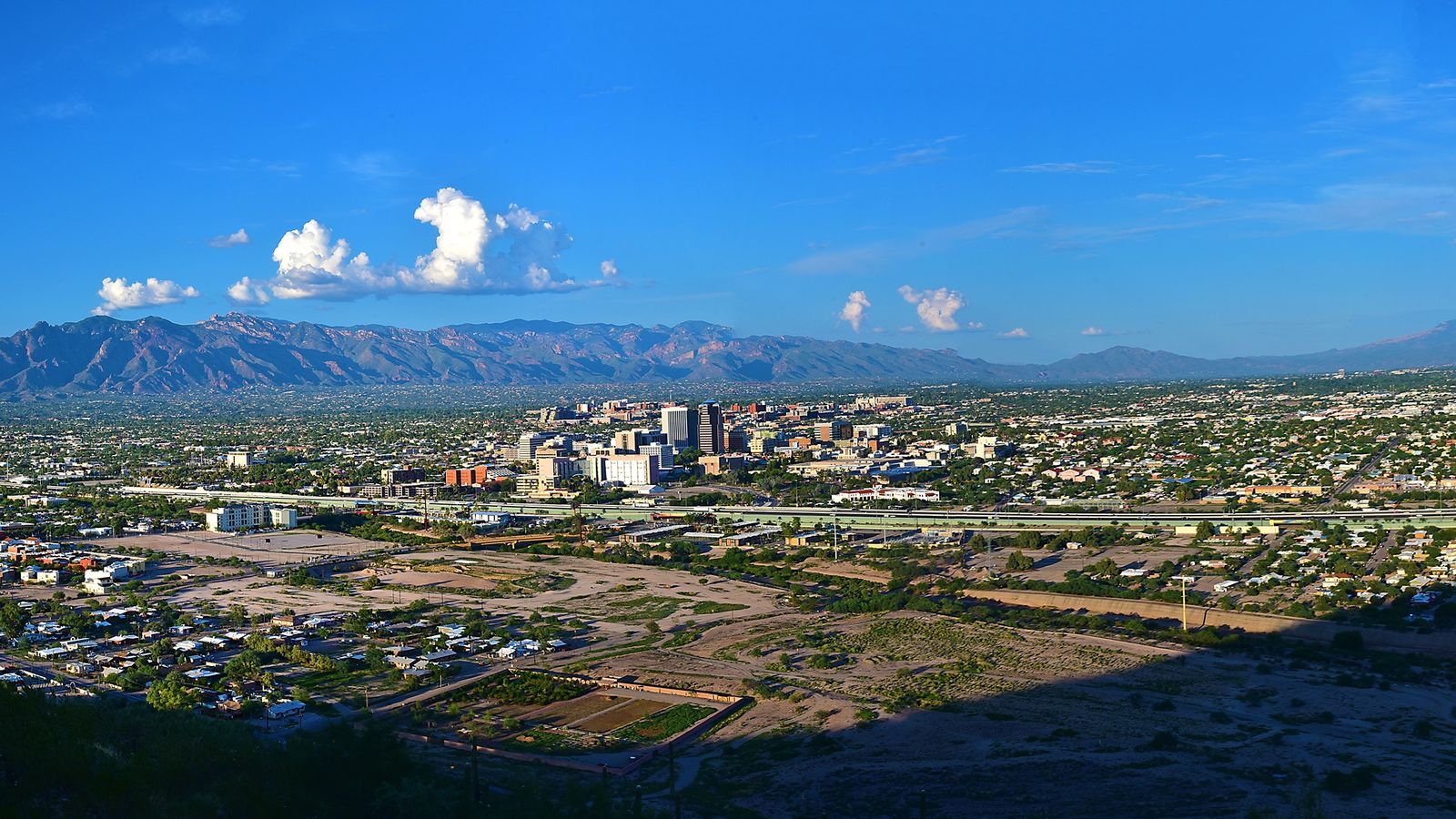 Downtown Tucson seen from Sentinel Peak, with the Santa Catalina Mountains rising behind the city under a blue sky.