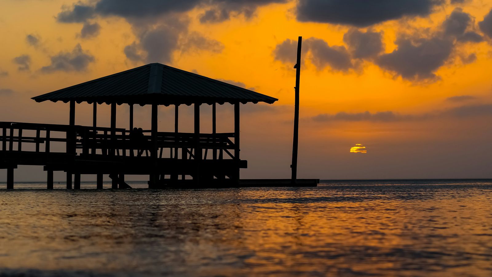 A covered pier and gazebo on Mobile Bay at Fairhope, in silhouette against an orange sunset.